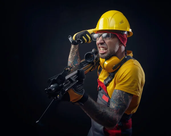 Een man in een bouwvakker uniform draagt een harde hoed met een airsoft wapen in zijn handen — Stockfoto