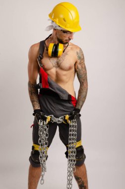 Beyaz atlı bir adam işçi tulumu ve uzun metal bir zincir tutan çıplak gövdeli bir şapka takıyor.