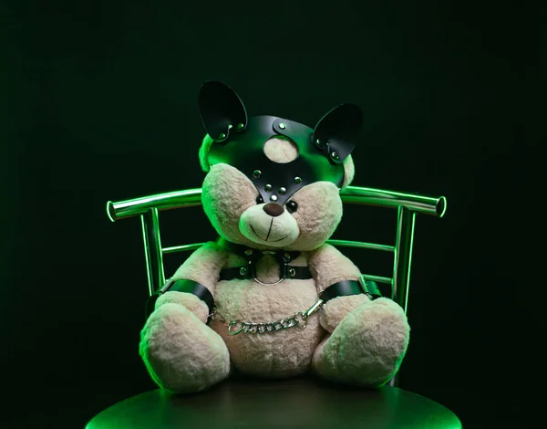 toy bear dressed in leather belts harness accessory for bdsm games on a dark background