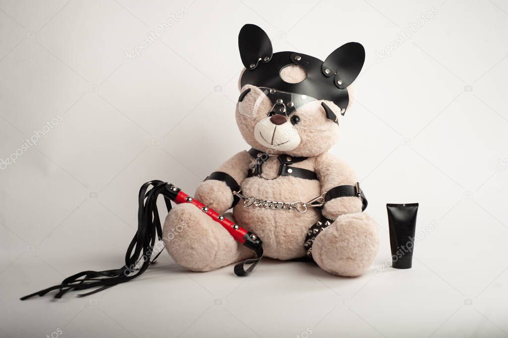 toy bear dressed in leather belts harness accessory for bdsm games on a light background