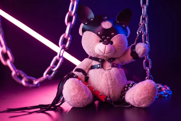 toy bear dressed in leather belts harness accessory for BDSM games on a dark background in neon light