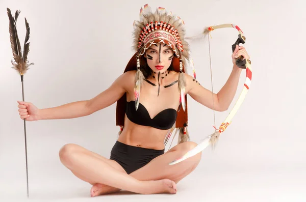 Girl in the image of indigenous peoples of America with a bow and arrow posing on a light background — Stock Photo, Image