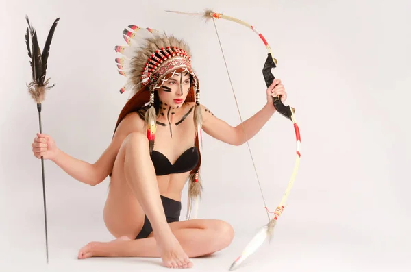 Girl in the image of indigenous peoples of America with a bow and arrow posing on a light background — Stock Photo, Image