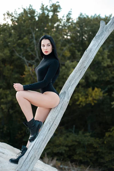 İnce, esmer, siyah elbiseli kadın, doğada cinsel poz veriyor.