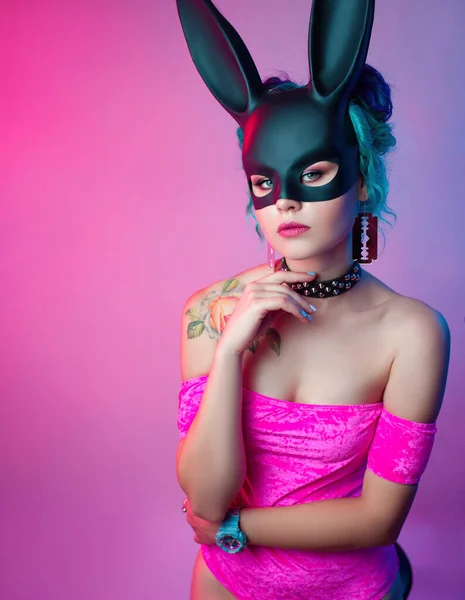 Una donna in un body rosa brillante e una maschera di coniglio posa su uno sfondo luminoso — Foto Stock
