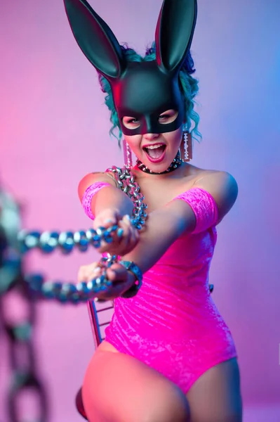A woman in a bright pink bodysuit and rabbit mask poses against a bright background with a chain — Stock Photo, Image