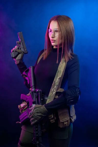 Eine Frau in militärischer Airsoft-Uniform mit amerikanischem Automatikgewehr und Pistole auf dunklem Hintergrund — Stockfoto