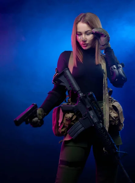 Una mujer en uniforme militar de airsoft con un rifle automático americano y una pistola sobre un fondo oscuro — Foto de Stock