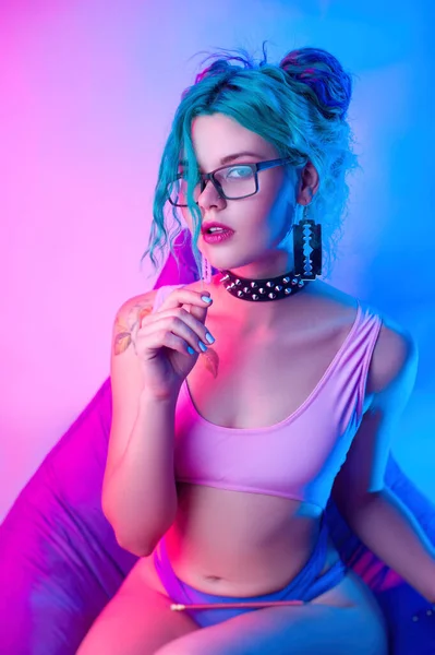 Una mujer sexy en un traje de baño brillante con pelo azul y gafas está sentado en una silla. — Foto de Stock