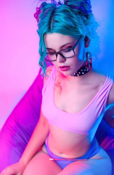 Una mujer sexy en un traje de baño brillante con pelo azul y gafas está sentado en una silla. —  Fotos de Stock