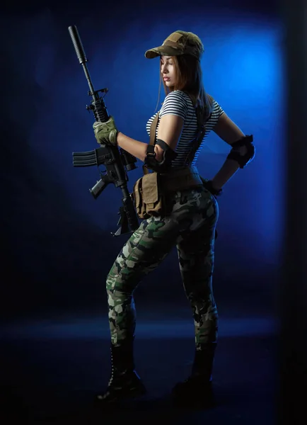 Uma mulher em um uniforme militar airsoft em um colete com um rifle automático americano em um fundo escuro — Fotografia de Stock