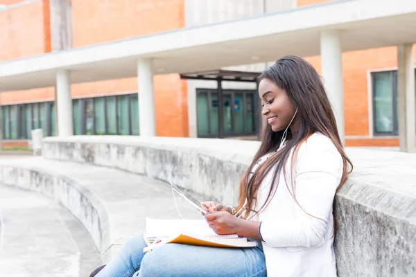アフリカの若い学生は イヤホンで音楽を聴いて 大学のキャンパスで勉強して笑顔 — ストック写真
