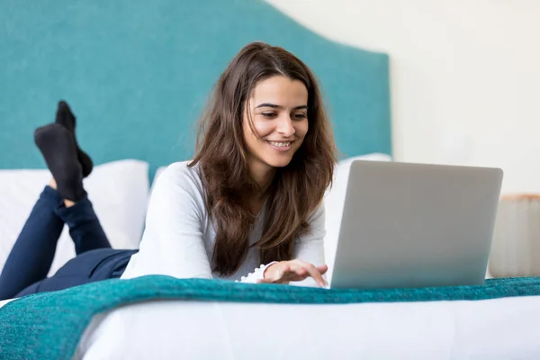微笑美丽的年轻女子使用笔记本电脑和躺在床上 — 图库照片