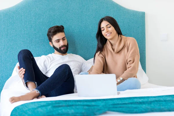 Happy couple watching on laptop screen while relaxing in bed