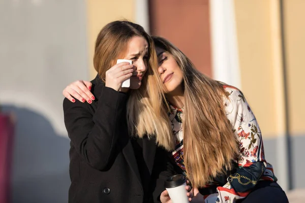 Young woman cheering up crying female friend at the street with unfocused background