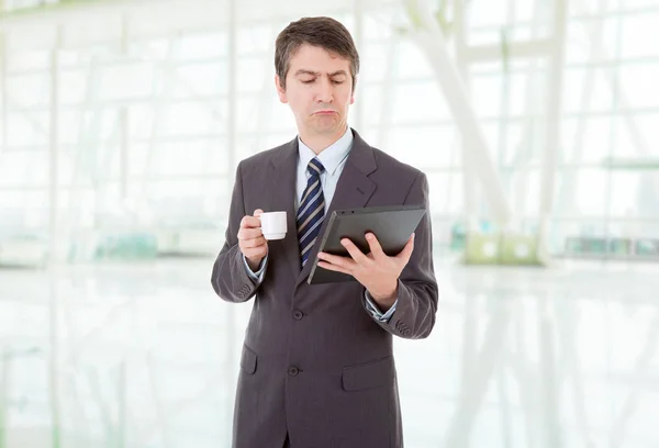 Portrait of a businessman looking at tablet pc and holding cup of coffee, at the office