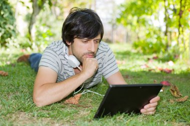 genç adam bir kulaklık ile müzik dinleme tablet pc ile rahatlatıcı bir parkta, açık