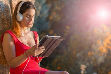 Bir tabletle çalışan sıradan bir kadın, kulaklıkla, açık havada.