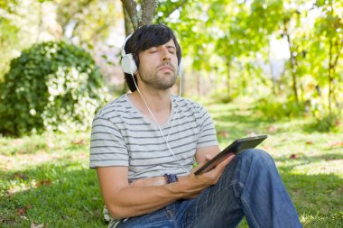 genç adam bir kulaklık ile müzik dinleme tablet pc ile rahatlatıcı bir parkta, açık