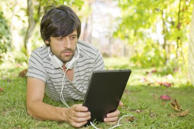 genç adam bir kulaklık ile müzik dinleme tablet pc ile rahatlatıcı bir parkta, açık
