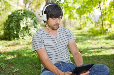 genç adam bir kulaklık ile müzik dinleme tablet pc ile rahatlatıcı bir parkta, açık