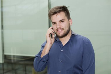 Bir ofis binasının içinde telefonla konuşan sıradan bir genç.