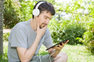 genç adam bir kulaklık ile müzik dinleme tablet pc ile rahatlatıcı bir parkta, açık