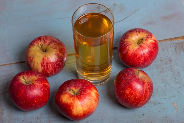 Glas Apfelsaft und rote Äpfel auf blauem alten Holzgrund — Stockfoto