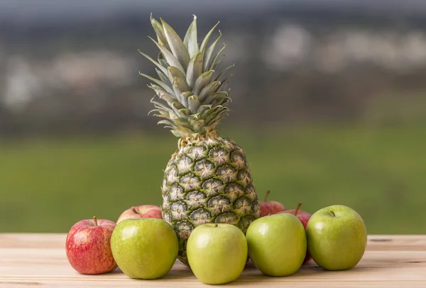 Ananas och äpple på bord av trä, utomhus — Stockfoto