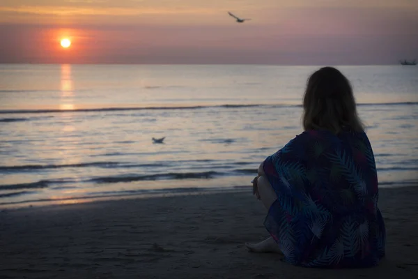 bir kadın sahilde oturan ve gün denizde seyir