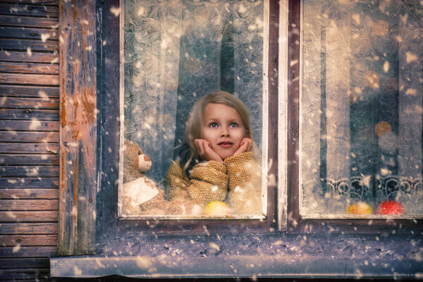 girl looks out the window at the falling snow