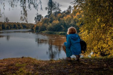 Yetişkin kadın gezgin sonbahar günü nehir kıyısında dinleniyor.
