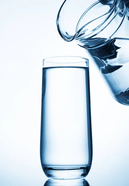 Gießen von Wasser aus Glaskannen auf blauem Hintergrund — Stockfoto