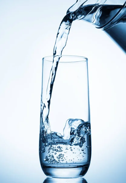 Versare acqua dalla brocca di vetro su sfondo blu — Foto Stock