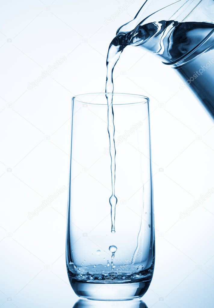 Pouring water from glass pitcher on blue background 