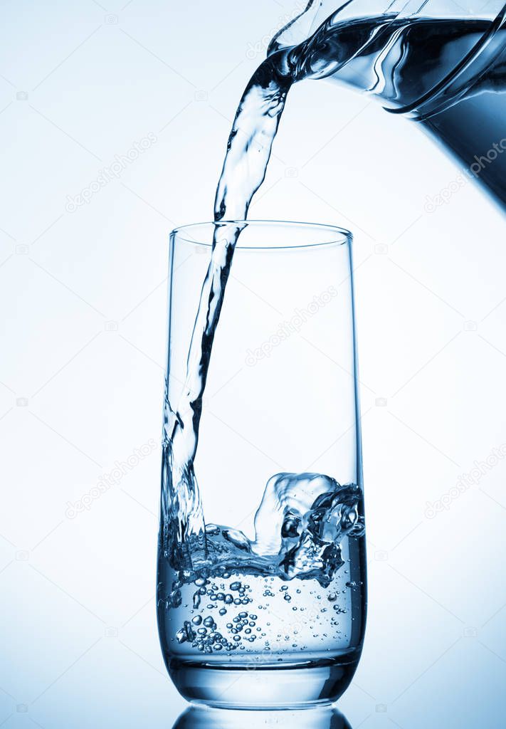 Pouring water from glass pitcher on blue background 