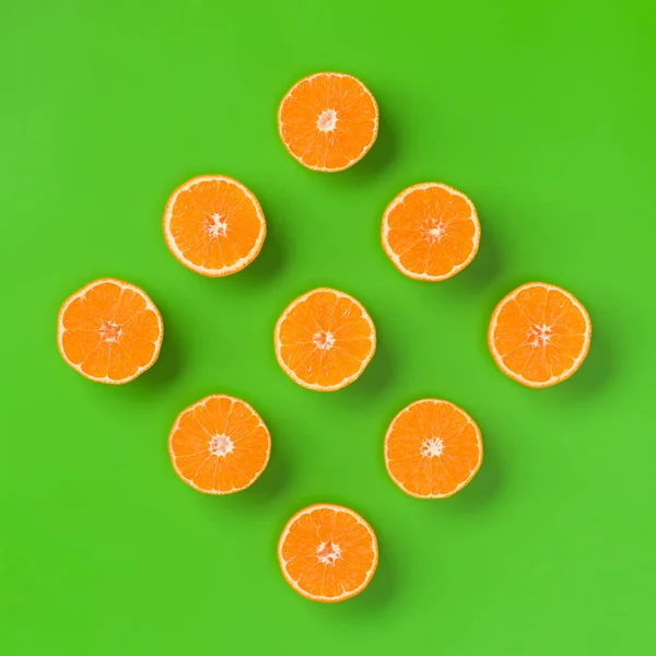 Fruit pattern of fresh orange slices on green background. Flat lay, top view. Pop art design, creative summer concept. Half of citrus in minimal style.