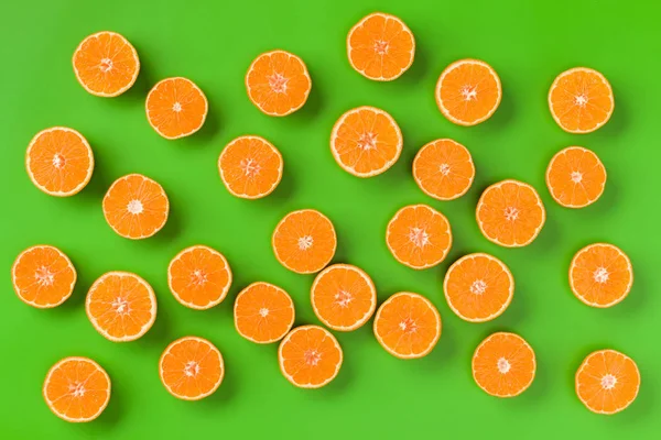 Fruit pattern of fresh orange slices on green background. Flat lay, top view. Pop art design, creative summer concept. Half of citrus in minimal style.