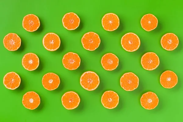 Fruit pattern of fresh orange slices on green background. Flat lay, top view. Pop art design, creative summer concept. Half of citrus in minimal style.