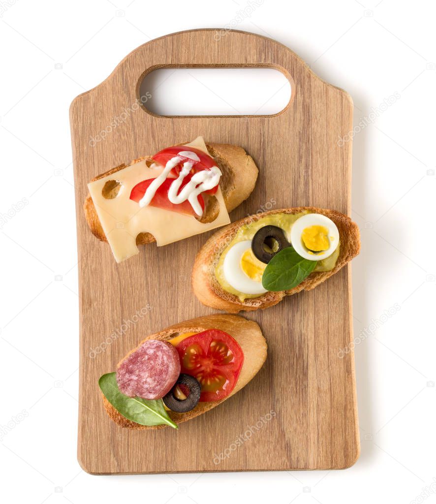 Open faced sandwich canape or crostini on a wooden serving board isolated on white background closeup. Top view.