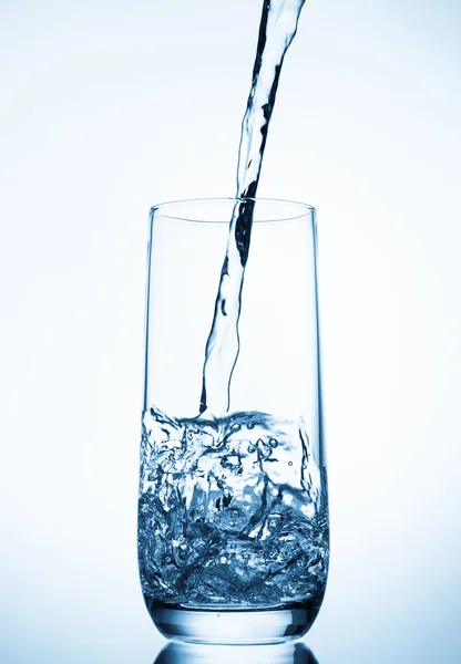 Acqua versando in vetro su sfondo blu — Foto Stock