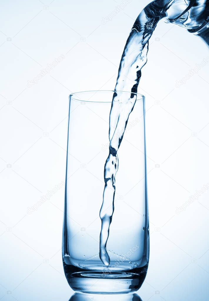 Pouring water from glass pitcher on blue background 