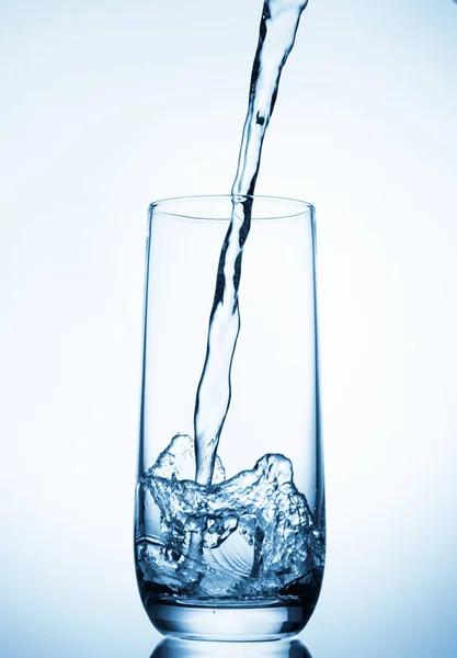 Wasser gießt in Glas auf blauem Hintergrund — Stockfoto