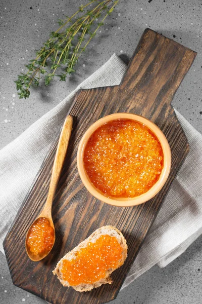 Red caviar in ceramic bowl on wooden Board on grey background. Top view — Stock Image Red Caviar Ceramic Bowl Wooden Board Grey Background Top View Royalty Free Stock Images