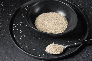 Sesame in black plate on dark background. Organic food for healthy eating