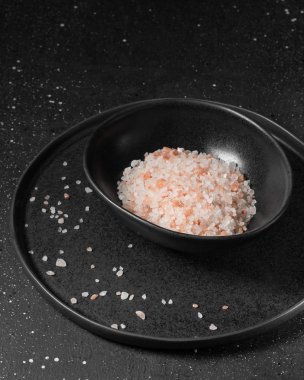 Karanlık bir arka plan üzerinde siyah bir tabak içinde pembe deniz tuzu