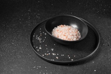 Karanlık bir arka plan üzerinde siyah bir tabak içinde pembe deniz tuzu