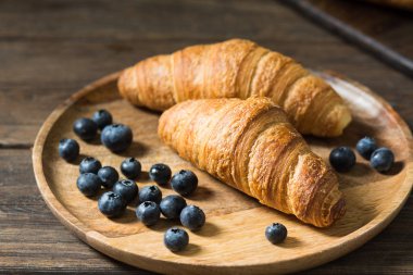 Ahşap bir masa üzerinde ahşap bir tabakta kruvasan. Rustik stil