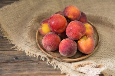 Ahşap bir masa üzerinde ahşap bir tabak üzerinde Şeftali. Rustik stil