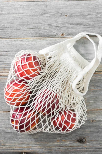 Juicy and ripe nectarines in mesh bag on grey wooden background